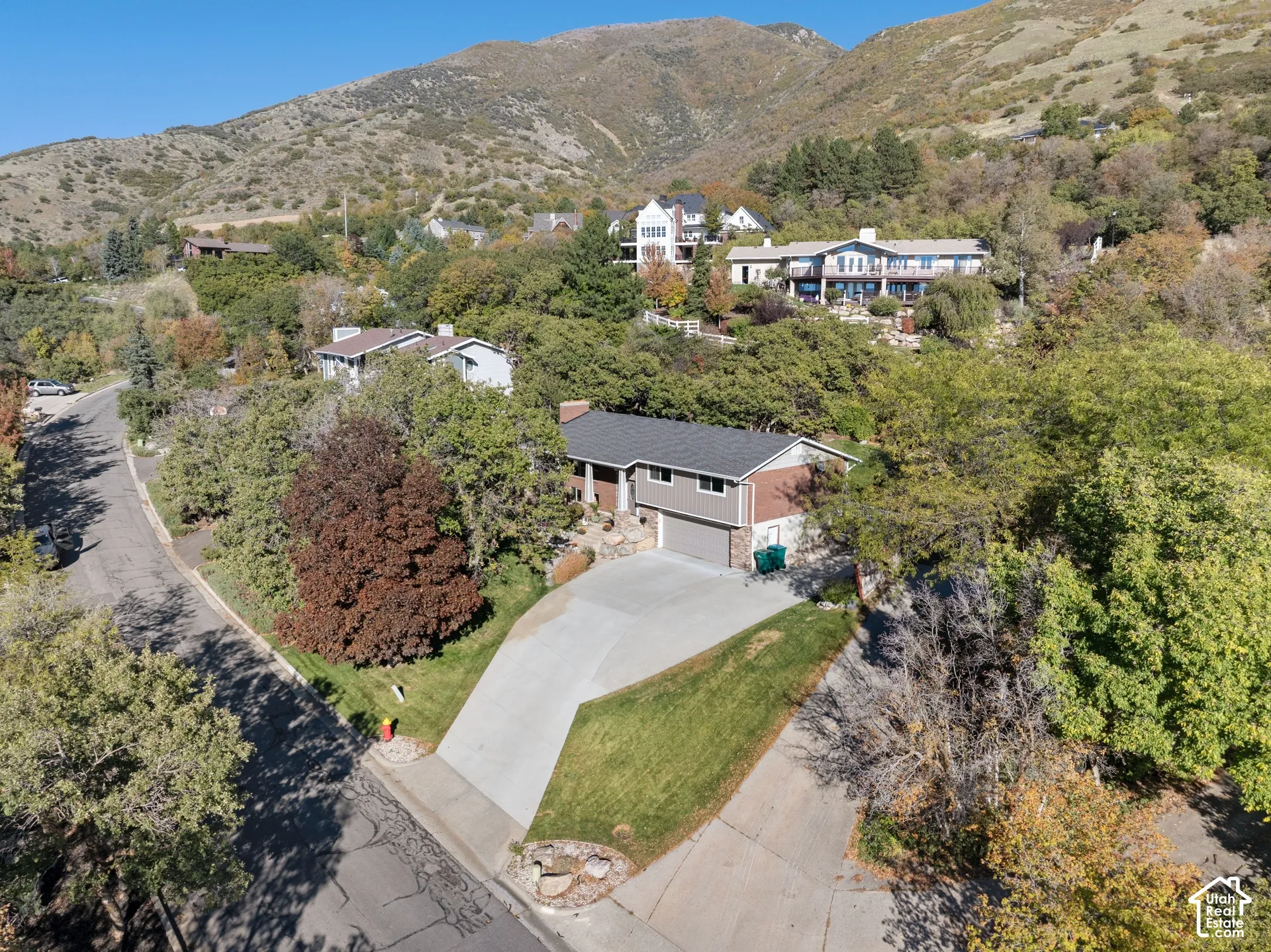 Multi-level residence featuring a concrete driveway, two-car garage, brick and siding exterior, asphalt shingled roof, and a sloped mountain backdrop