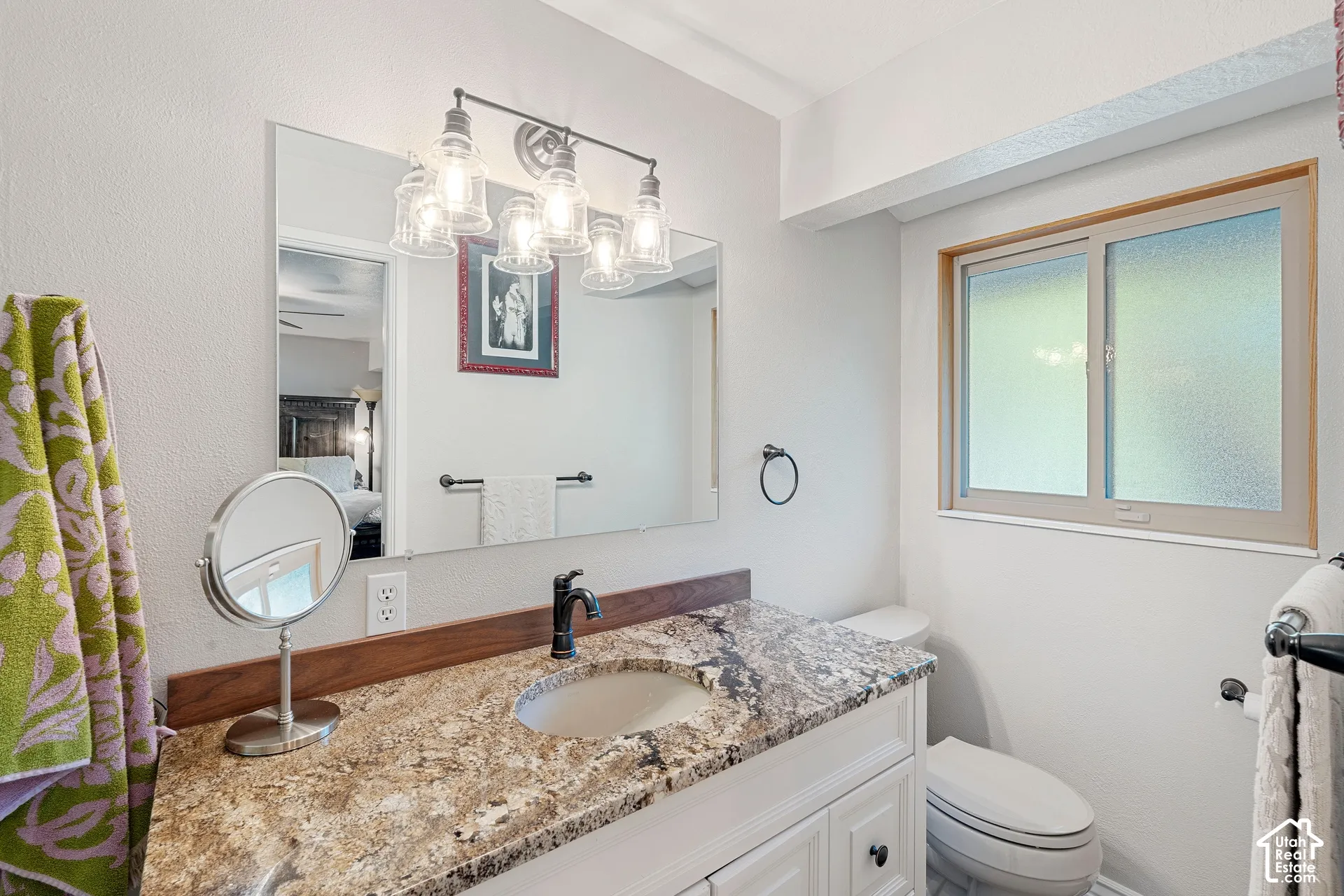 Vanity featuring a stone countertop with wood-trim backsplash, undermount sink, multi-bulb light fixture, and framed wall mirror