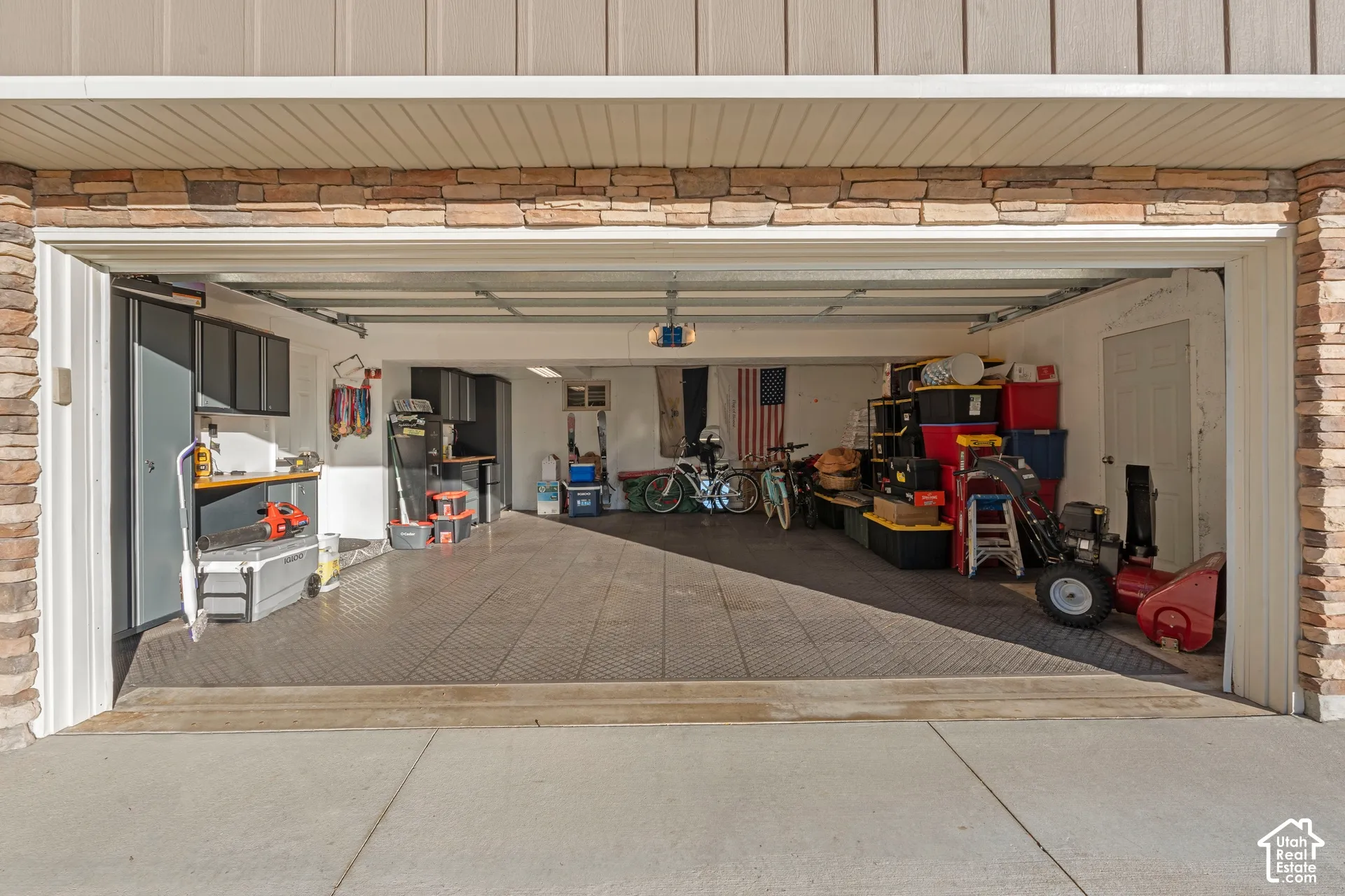 Attached two-car garage featuring stacked stone veneer siding, modular floor tiles, and built-in wall-mounted cabinetry