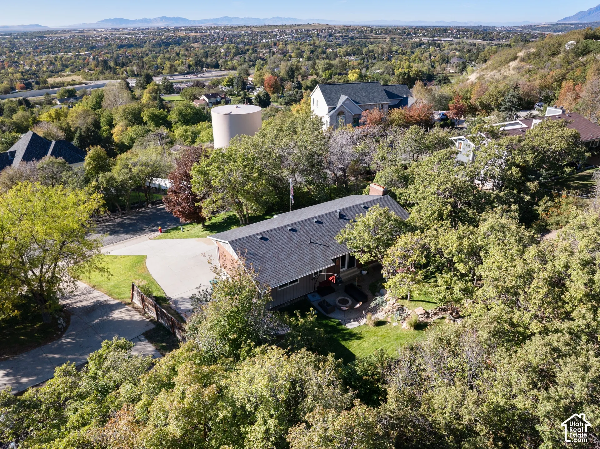 Aerial perspective of a multi-story residence featuring a shingled roof, concrete driveway, stone-accented hardscaping, and mature landscaping