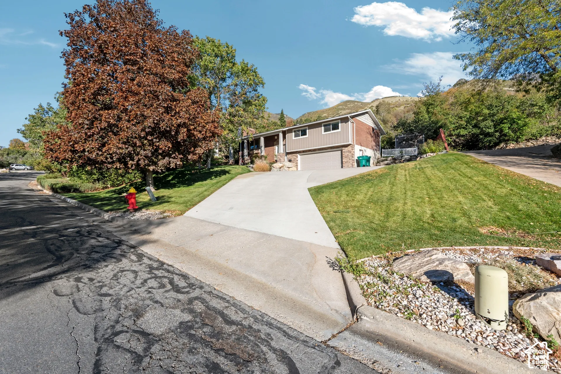 Split-level exterior featuring brick and siding facade, two-car garage, concrete driveway, and landscaped lawn with mature trees