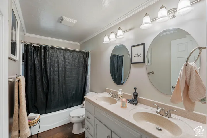 Dual-sink vanity with a solid-surface countertop, twin oval wall-mounted mirrors, two triple-light fixtures, and wood-finish flooring