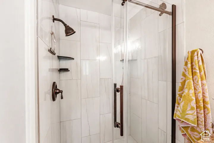 Walk-in shower featuring floor-to-ceiling rectified porcelain tile, bronze-finish fixtures, dual built-in corner shelving, and a frameless glass sliding enclosure