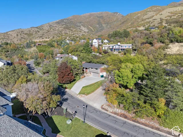 Residential property featuring a concrete driveway, attached garage, and mature tree-lined landscaping, set against a mountainous backdrop