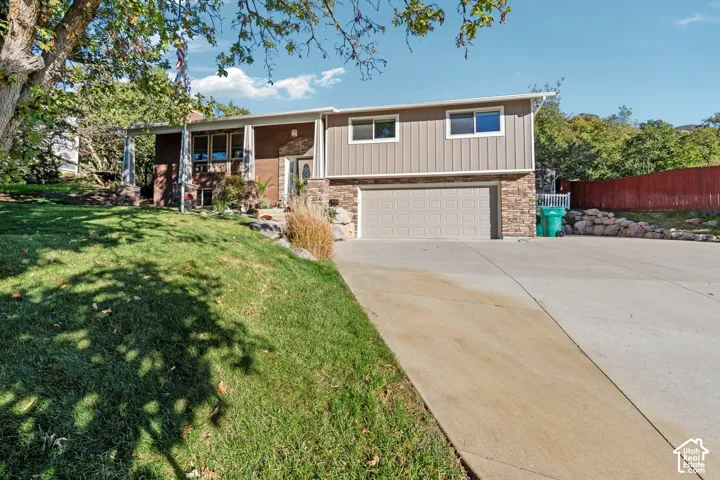 Multi-level exterior featuring a brick and stone facade, vertical metal siding, attached two-car garage, and concrete driveway