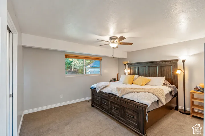 Bedroom featuring neutral wall paint, carpeted flooring, a ceiling fan with integrated lighting, and a single-pane window with wood-finish blinds