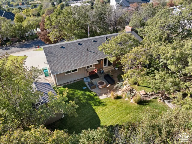 Aerial perspective featuring a shingled roofline, manicured lawn, stone-accented hardscaping, and mature trees