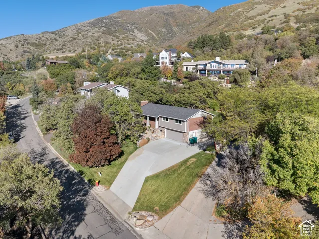 Multi-level residence featuring a concrete driveway, two-car garage, brick and siding exterior, asphalt shingled roof, and a sloped mountain backdrop