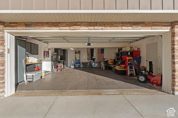 Attached two-car garage featuring stacked stone veneer siding, modular floor tiles, and built-in wall-mounted cabinetry