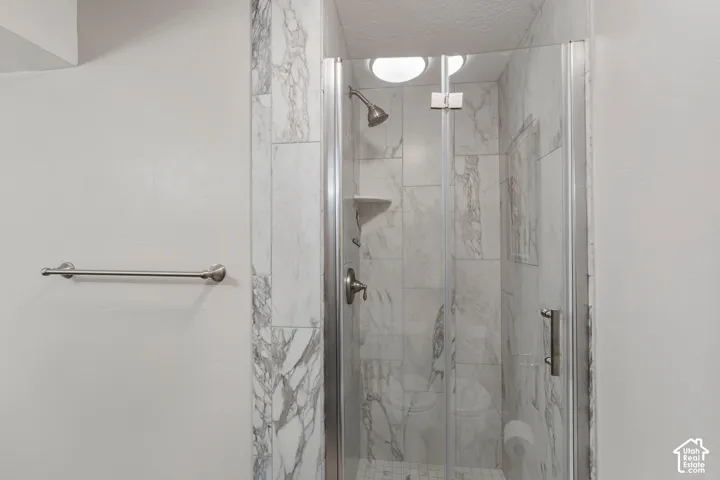 Walk-in shower featuring marble-patterned tile surround, glass pivot door, built-in corner shelving, and metal hardware