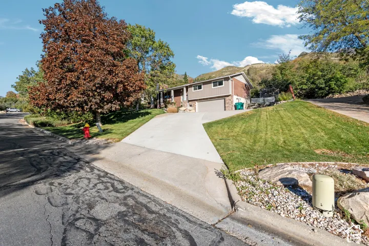 Split-level exterior featuring brick and siding facade, two-car garage, concrete driveway, and landscaped lawn with mature trees