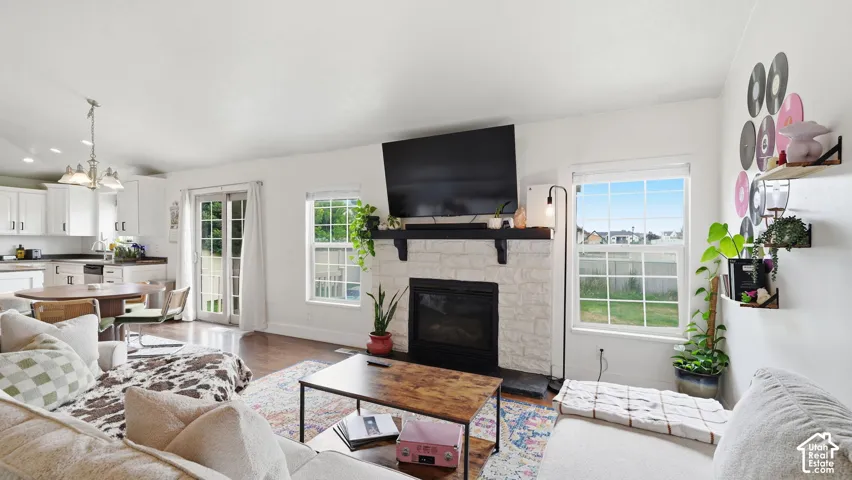 Living area featuring wood-finish flooring, a stone-surround fireplace with a wooden mantel, multi-pane windows, and glass patio doors