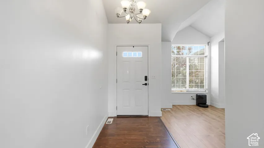 Foyer featuring wood-finish flooring, vaulted ceilings, a multi-light chandelier, and an exterior door with an inset glass pane