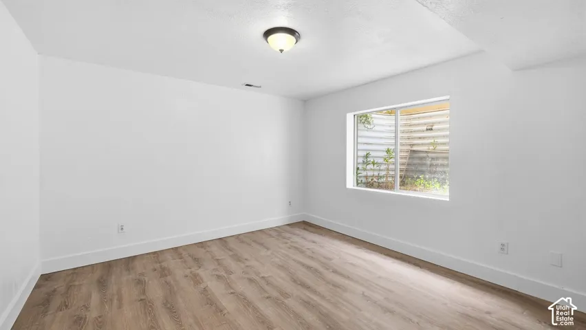 Room with neutral paint, wood-finish flooring, flush-mount ceiling lighting, and a sliding window with an integrated window well