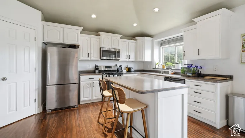 Kitchen featuring white cabinetry, wood-finish flooring, stainless steel appliances, a center island with countertop seating, and recessed lighting