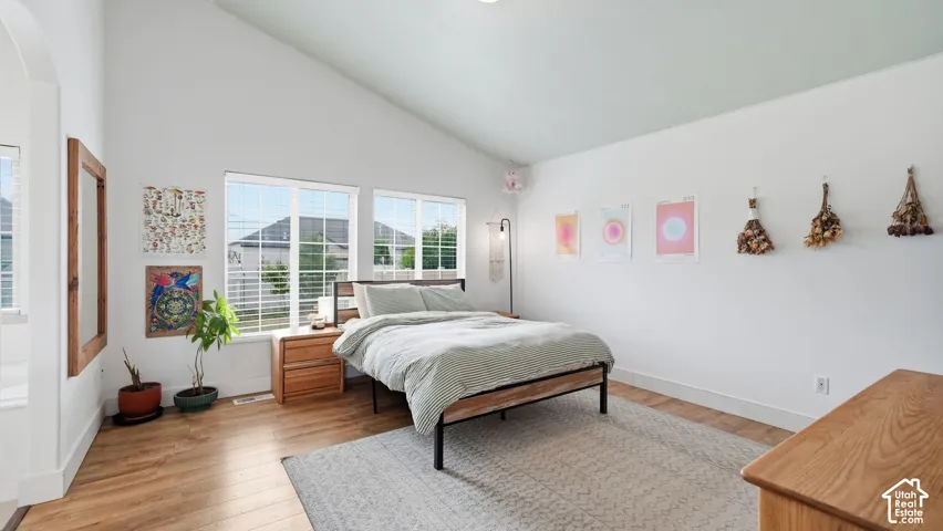 Vaulted ceiling, wood-finish flooring, and multiple windows with horizontal blinds