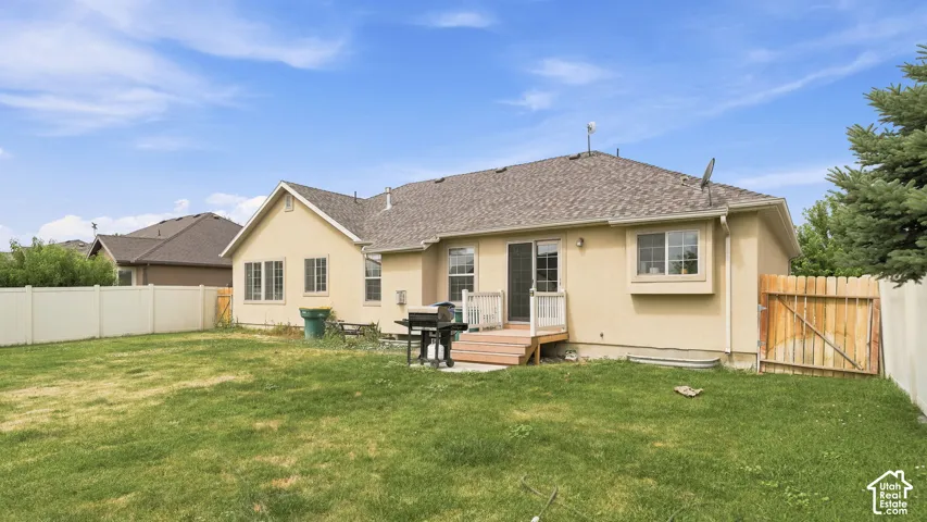 Backyard featuring a grass lawn, perimeter vinyl fencing, and a wood-deck platform with stairs