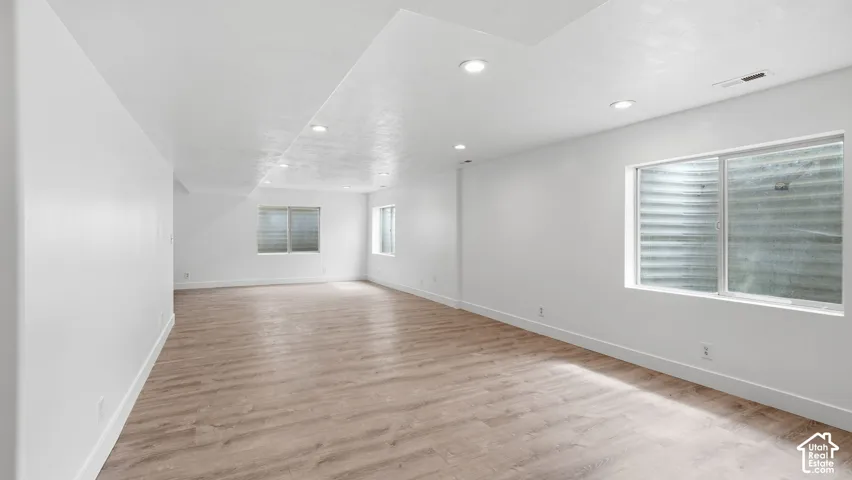 Interior space featuring recessed lighting, wood-finish flooring, and multiple egress windows with corrugated steel wells