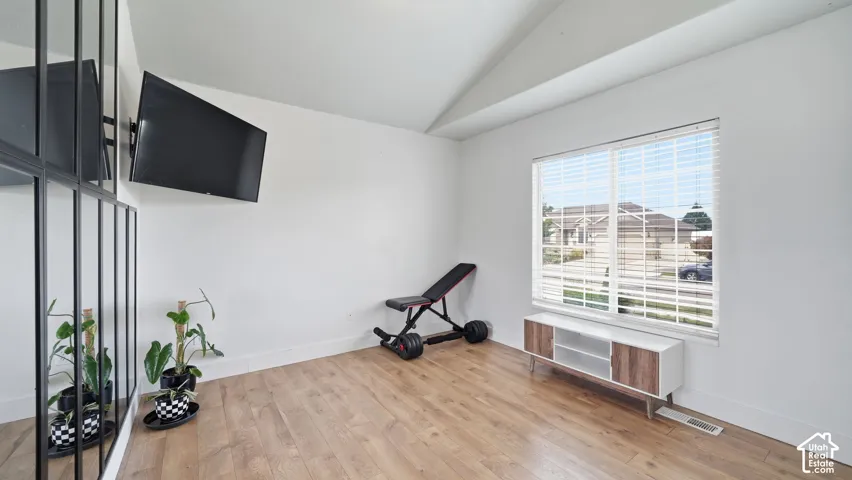 Vaulted ceiling, wood-finish flooring, and a floor-to-ceiling multi-panel decorative mirror wall