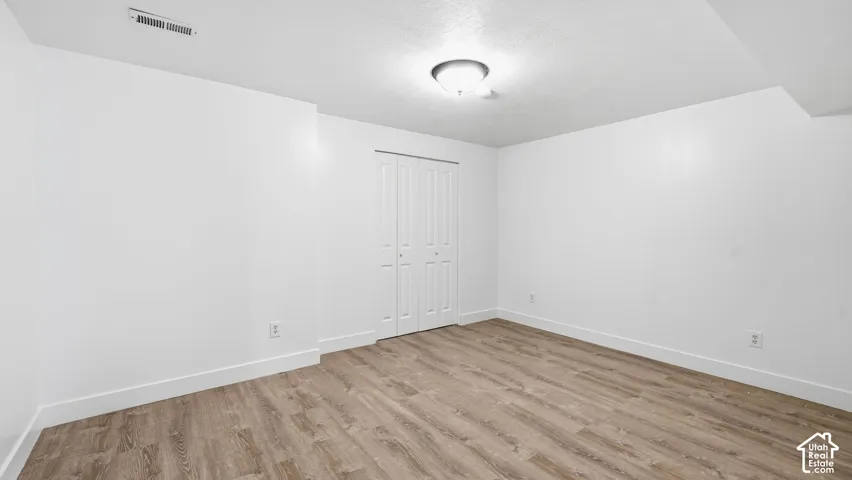 Room featuring wood-finish flooring, white walls, and a closet with bifold doors