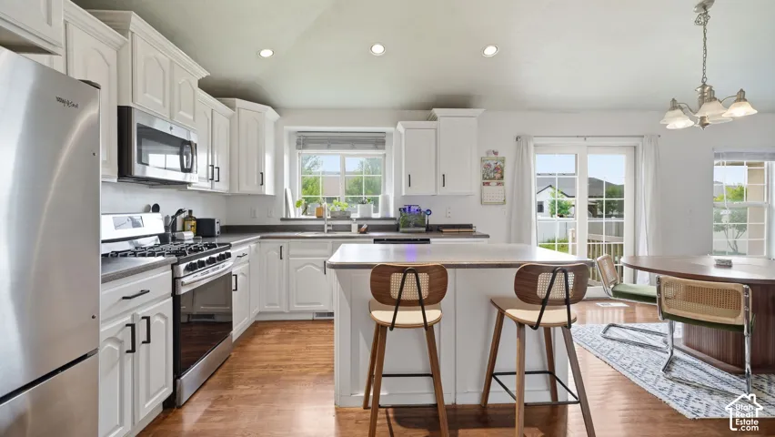 Kitchen featuring white cabinetry, center island with stone-surface countertop, stainless steel appliances, wood-finish flooring, and recessed lighting