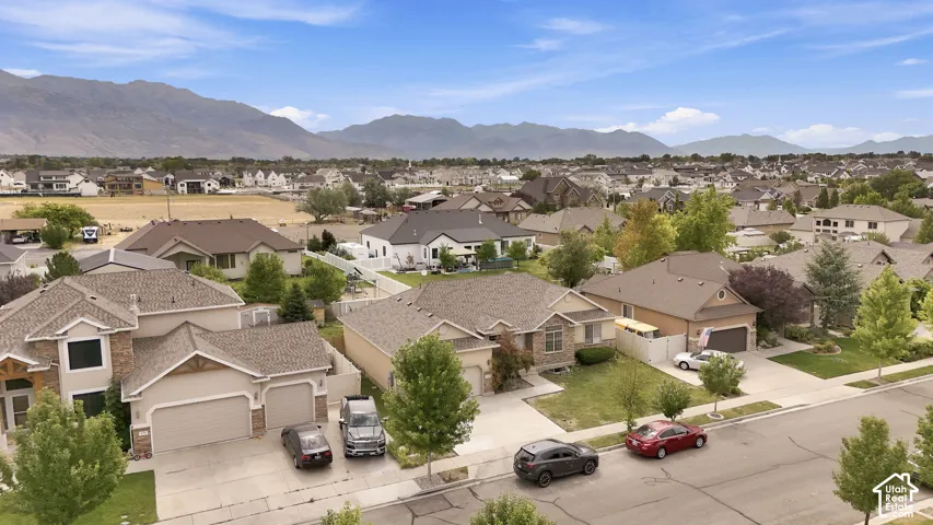 Aerial perspective featuring residential lots with paved driveways, manicured lawns, mature trees, and a mountain range backdrop