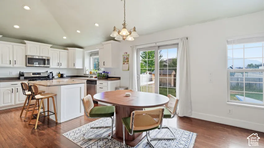 Vaulted ceiling, kitchen featuring white cabinetry, central island with countertop, wood-finish flooring, and sliding glass door