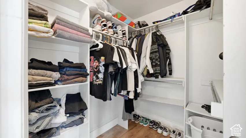 Custom closet featuring white built-in shelving, multi-level hanging rods, and wood-finish flooring