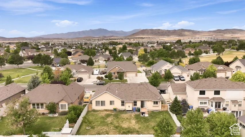 Aerial perspective of a suburban neighborhood featuring a residential lot with a fenced backyard and a prominent mountain range backdrop