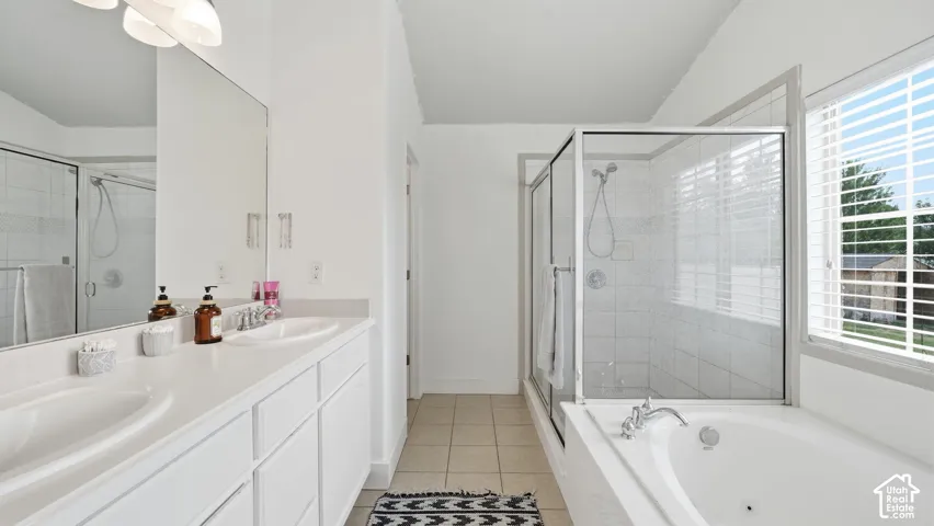 Bathroom featuring a dual-sink vanity with a solid-surface countertop, a separate glass-enclosed shower, a jetted soaking tub, and ceramic tile flooring