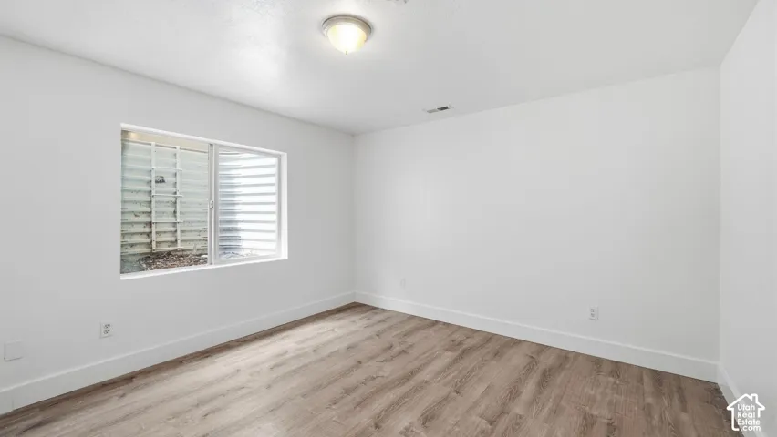 Room featuring wood-finish flooring, white walls, a flush-mount ceiling light fixture, and an egress window with a metal window well