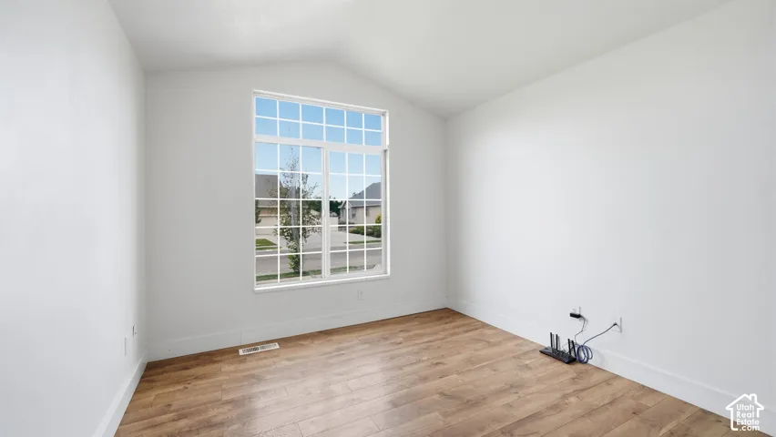 Vaulted ceiling, wood-finish flooring, and a large window with a transom light