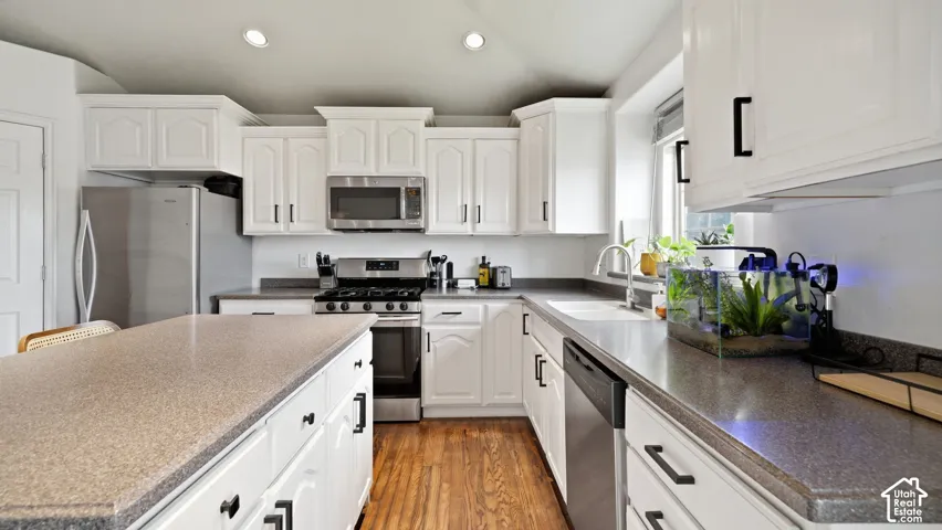 Kitchen featuring white cabinetry, solid-surface countertops, center island, stainless steel appliances, and wood-finish flooring