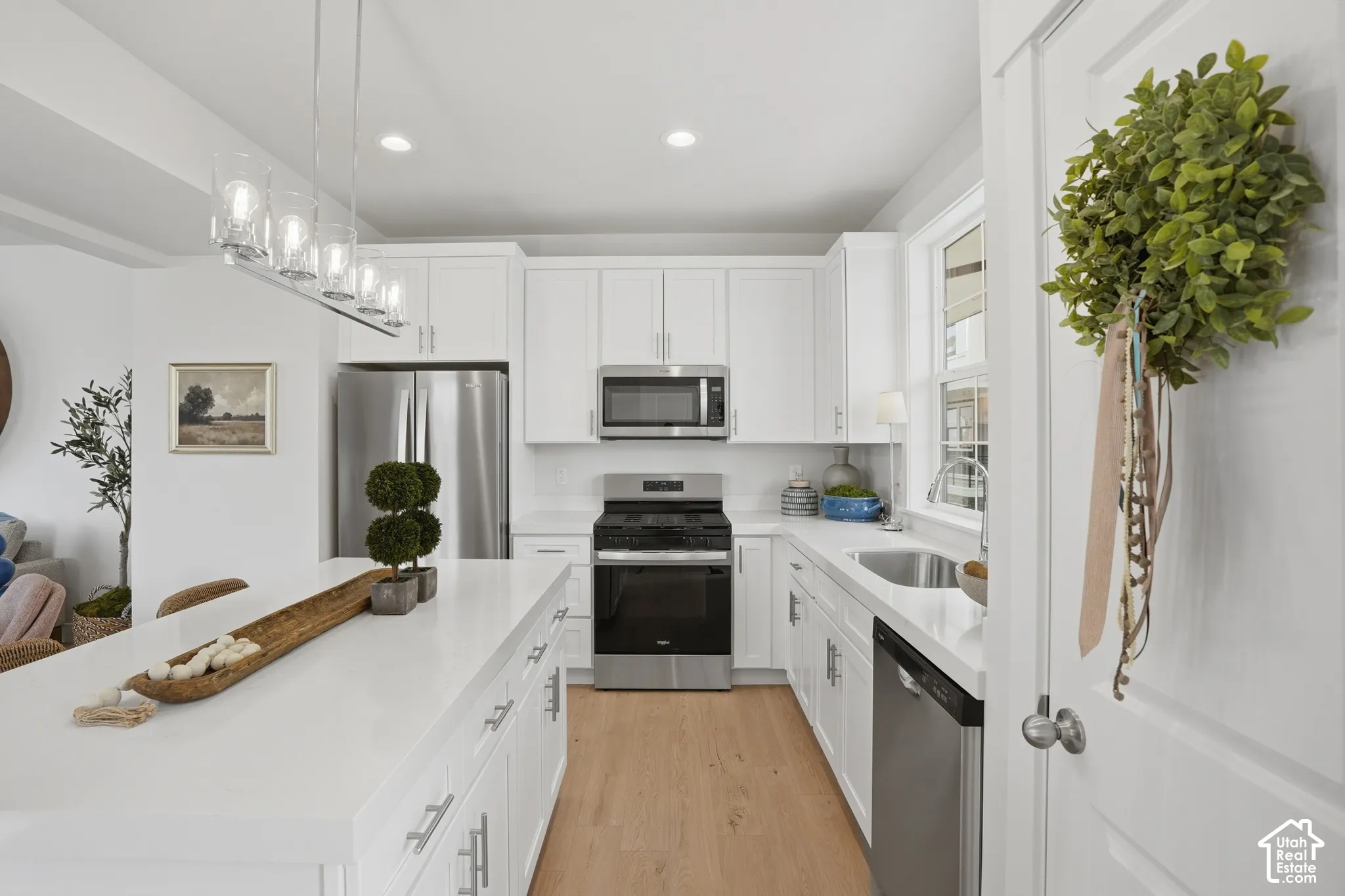 Kitchen featuring white shaker-style cabinetry, quartz countertops, wood-finish flooring, stainless steel appliances, and a central island with pendant lighting