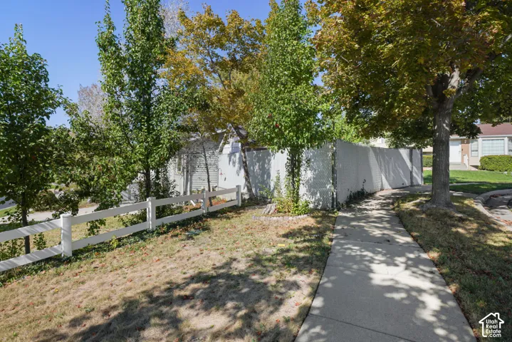 Exterior lot featuring a concrete sidewalk, white vinyl fencing, and mature trees