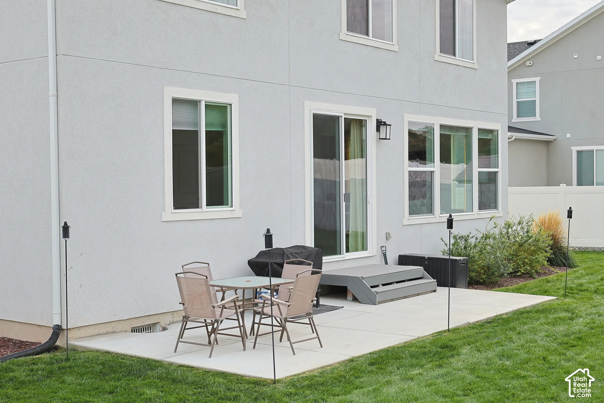 Rear exterior featuring a concrete patio, sliding glass door, tiered steps, dual-pane windows, and a landscaped lawn
