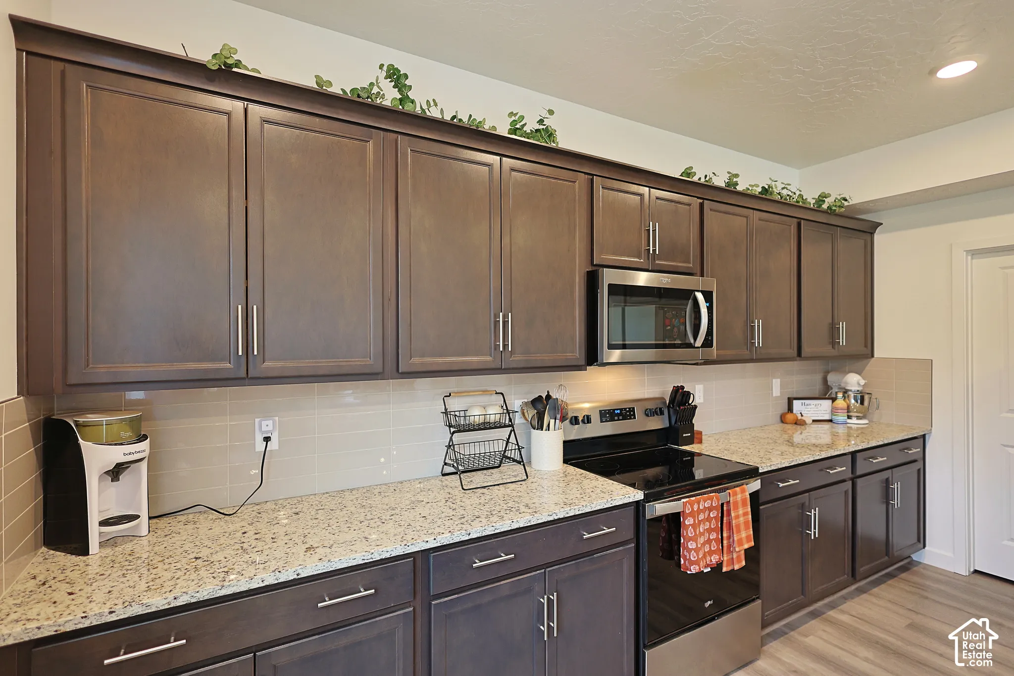 Dark wood cabinetry with brushed nickel hardware, stone-composite countertops, ceramic tile backsplash, and built-in stainless steel microwave