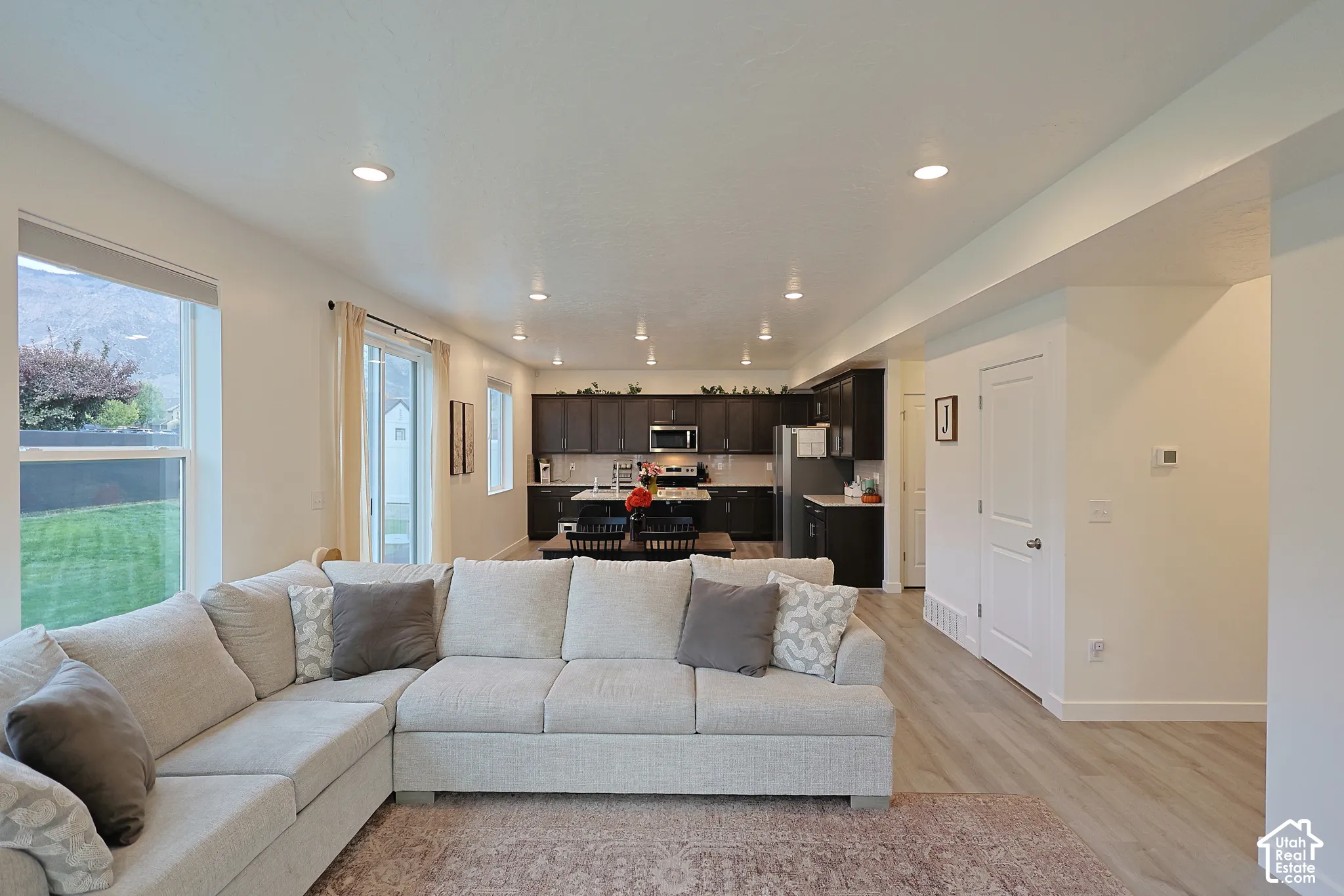 Open-concept interior featuring recessed lighting, wood-finish flooring, dark-toned cabinetry, and sliding glass doors with exterior access