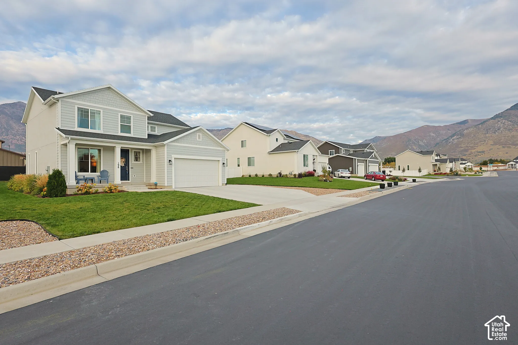 Two-story residence featuring light-colored horizontal siding, a covered front entryway, attached two-car garage, and mountain backdrop