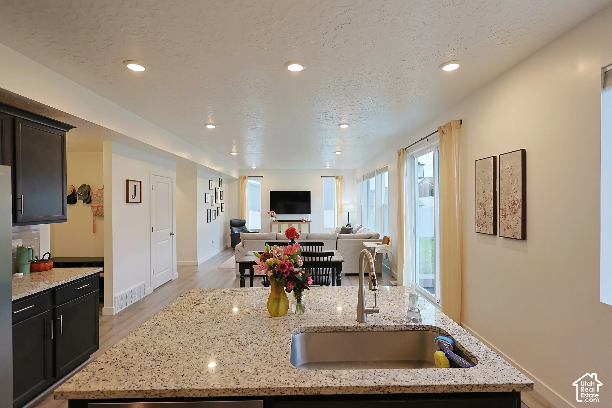 Kitchen island featuring stone countertops, an undermount stainless steel sink, and a gooseneck faucet, complemented by dark cabinetry, recessed lighting, and wood-finish flooring