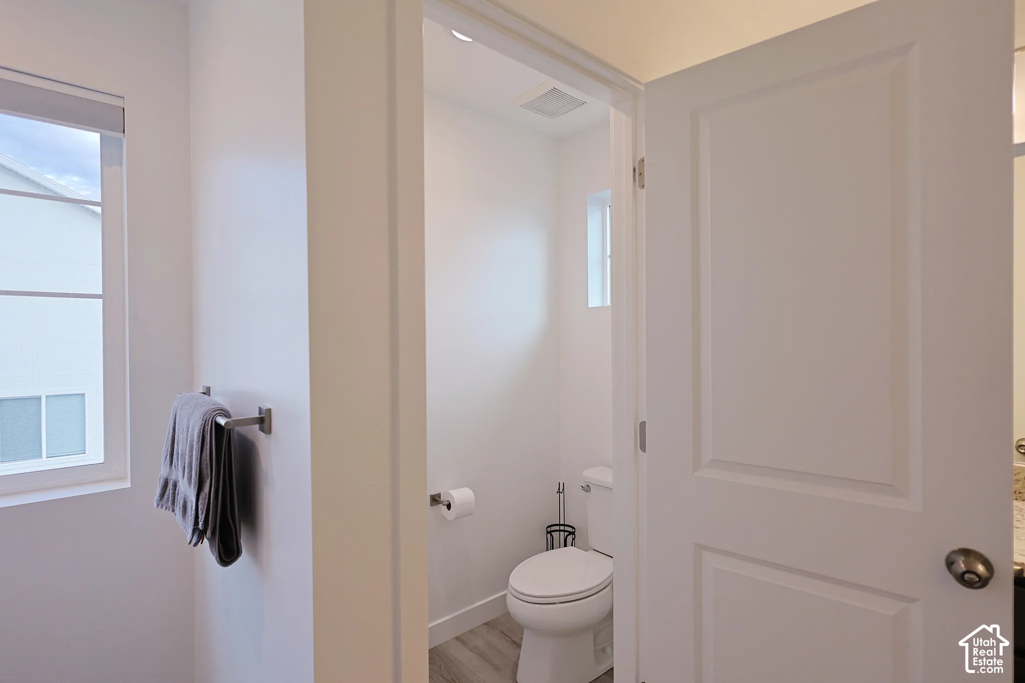 Enclosed bathroom featuring white walls, two-panel interior door, recessed lighting, and wood-finish flooring