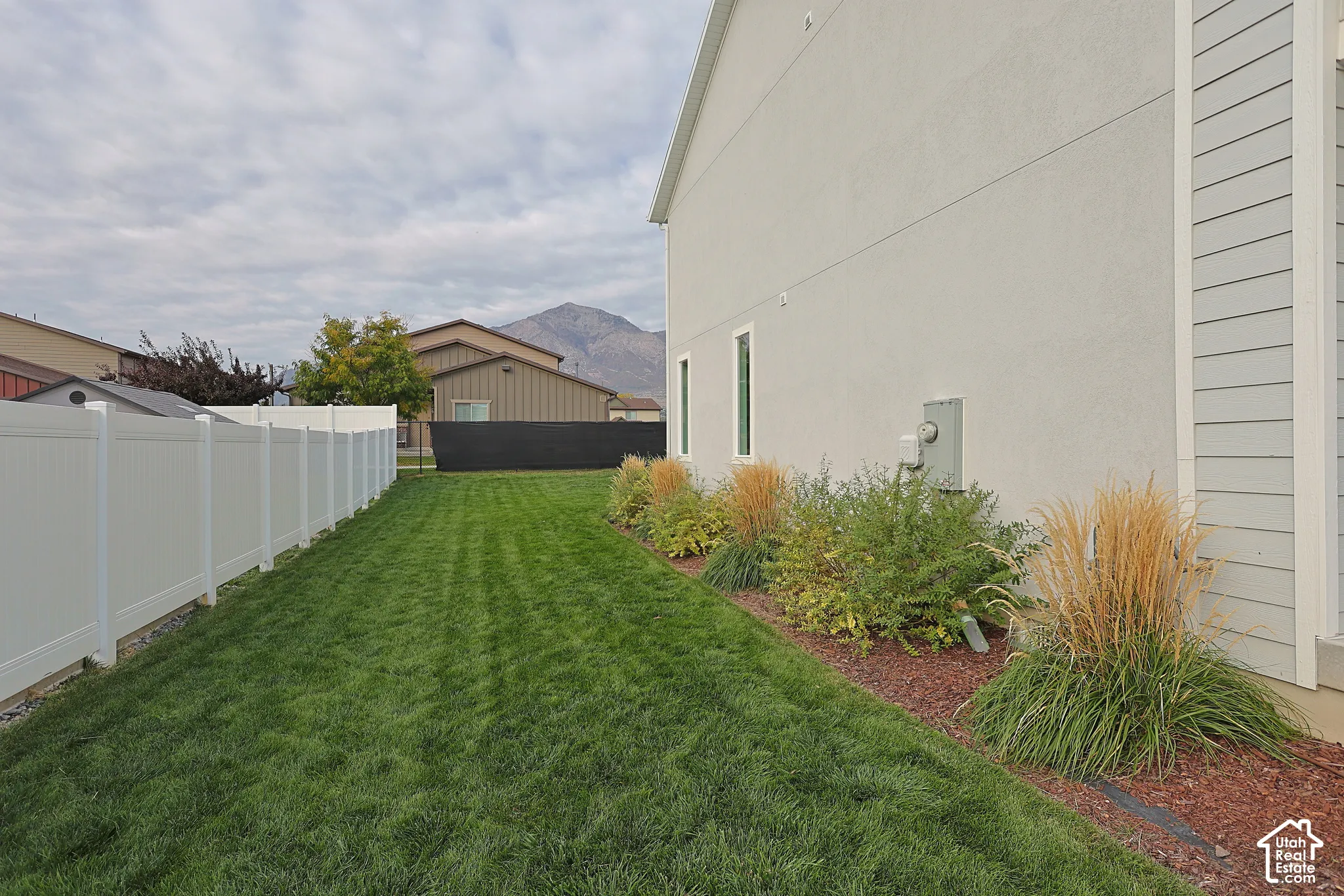 Side yard featuring a manicured lawn, white vinyl fencing, ornamental grasses, and mountain backdrop