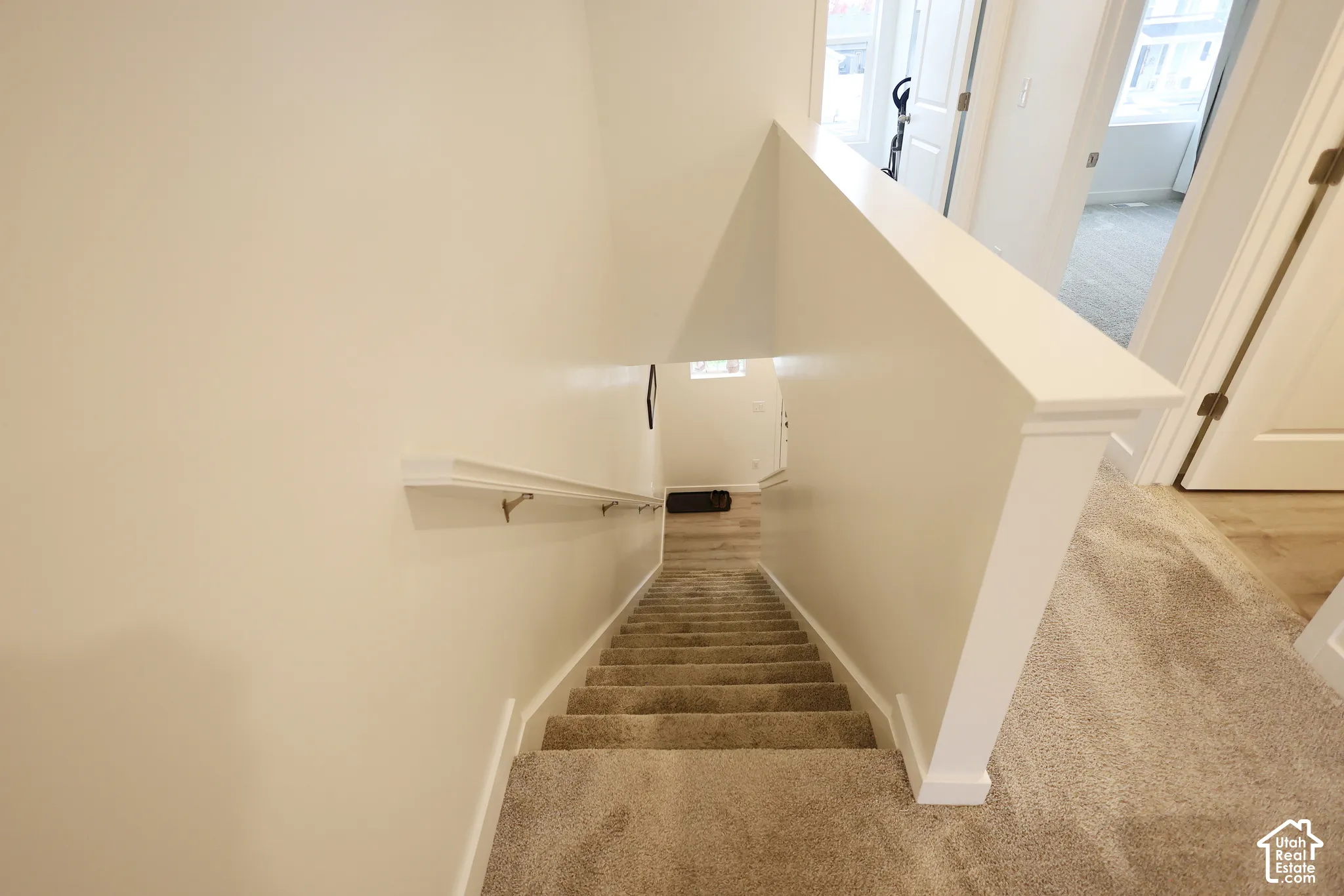 Staircase featuring neutral-toned carpeting, a white painted half-wall, and a mounted handrail