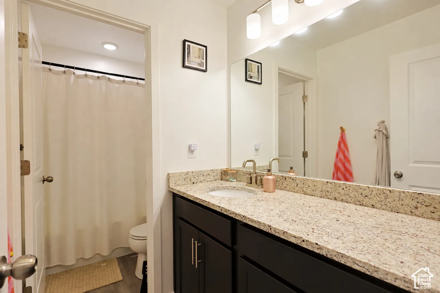 Dark cabinetry vanity featuring a stone-composite countertop, undermount sink, brushed nickel faucet, large wall-mounted mirror, and multi-bulb vanity light fixture