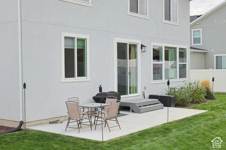 Rear exterior featuring a concrete patio, sliding glass door, tiered steps, dual-pane windows, and a landscaped lawn