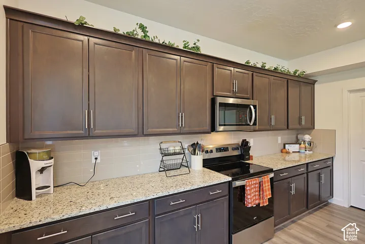 Dark wood cabinetry with brushed nickel hardware, stone-composite countertops, ceramic tile backsplash, and built-in stainless steel microwave