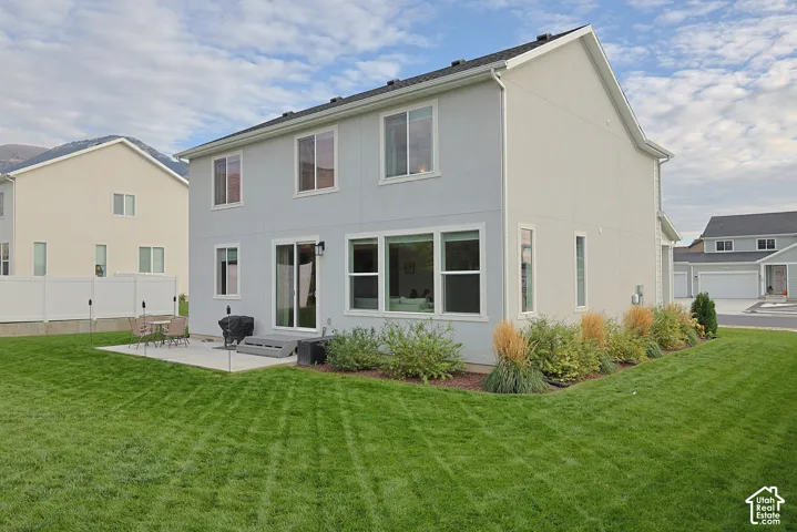 Two-story residence exterior featuring light-toned siding, a concrete patio, large multi-pane windows, sliding glass doors, and a manicured lawn with structured landscaping