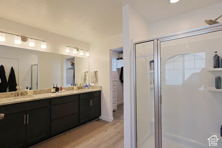 Double vanity with stone-surface countertop, dark cabinetry, full-width vanity mirror, dual vanity lighting fixtures, and walk-in shower with integrated shelving