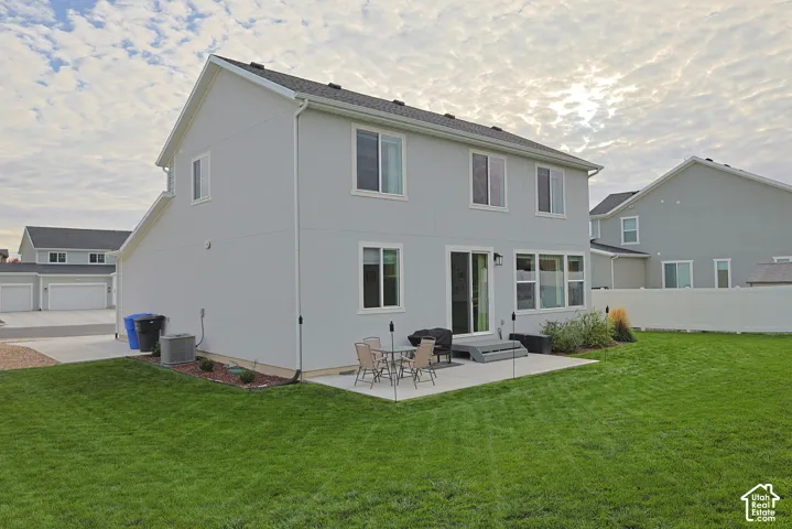 Two-story exterior featuring light-toned siding, a concrete patio, a rear sliding glass door, and a private fenced yard with a level lawn