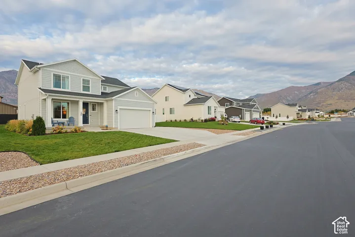 Two-story residence featuring light-colored horizontal siding, a covered front entryway, attached two-car garage, and mountain backdrop